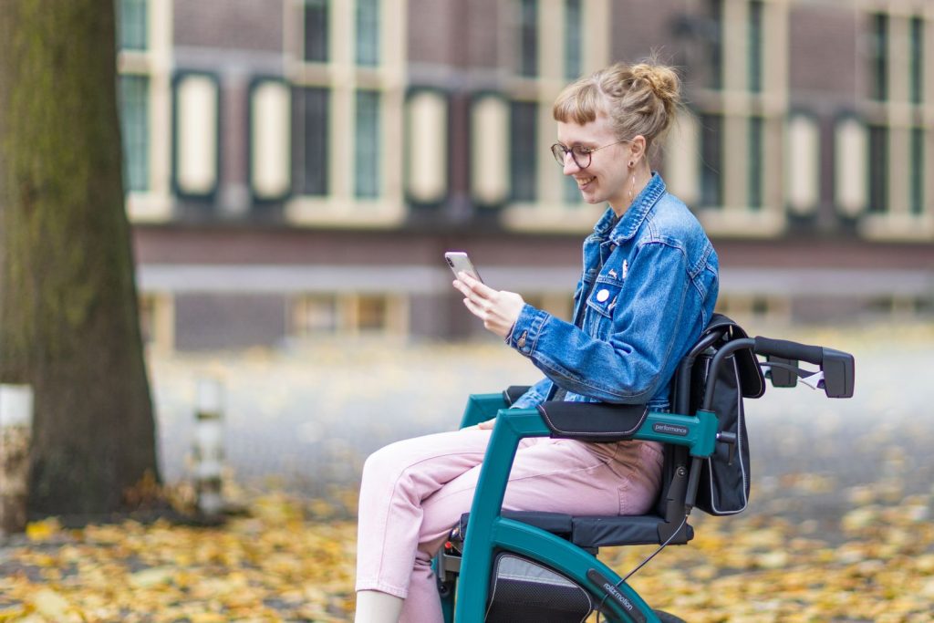 Mujer usuaria de silla de ruedas utiliza su teléfono móvil en un parque.