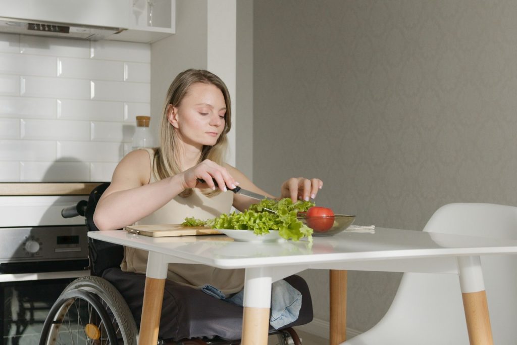 Mujer usuaria de silla de ruedas prepara alimentos en una cocina luminosa.